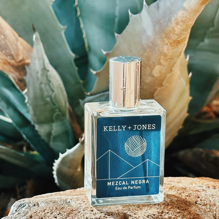 Kelly + Jones Mezcal Negra eau de parfum bottle on a rock with cacti in the background.
