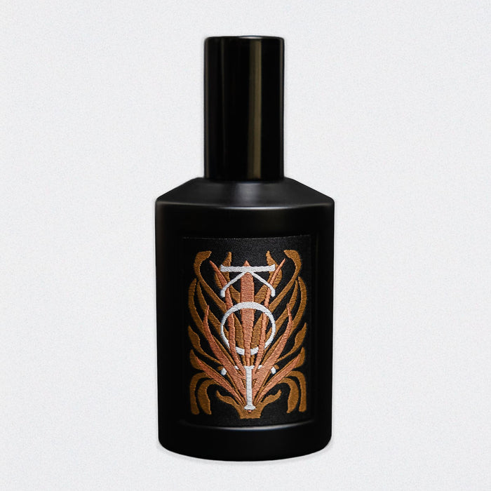 A black cylindrical bottle of Fischersund KOT fragrance with a matching black cap, featuring a front label with a stylized metallic gold and silver emblem, set against a white background.