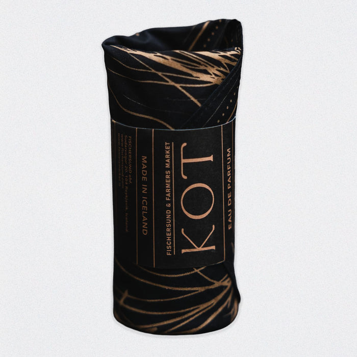 A rolled black bandana with a gold pattern covering a bottle of Fischersund KOT fragrance. The rolled bottle appears on a white background.